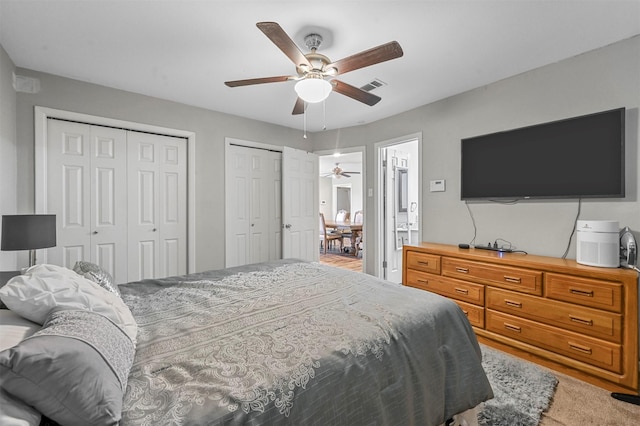 carpeted bedroom featuring ceiling fan and multiple closets