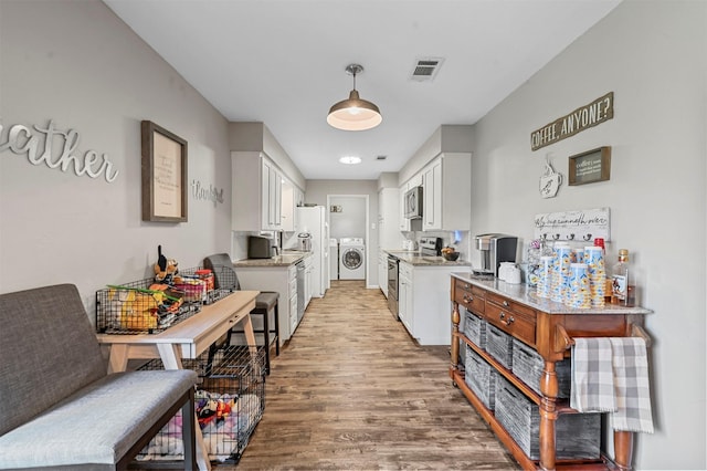 kitchen featuring washer and dryer, light wood-type flooring, white cabinetry, and appliances with stainless steel finishes