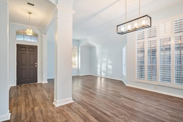 entrance foyer with ornate columns, dark wood-type flooring, and a notable chandelier