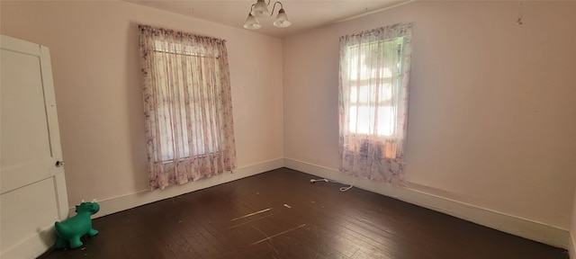 empty room with dark hardwood / wood-style floors and an inviting chandelier