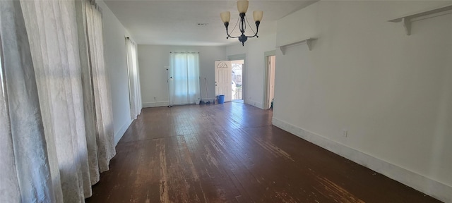 spare room featuring dark wood-type flooring and a chandelier