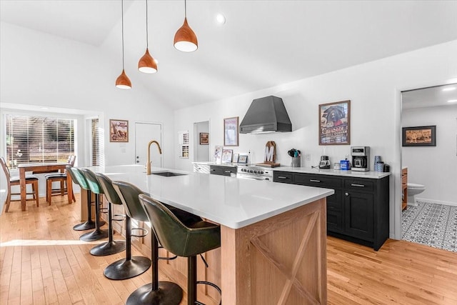 kitchen with decorative light fixtures, sink, a kitchen breakfast bar, light hardwood / wood-style floors, and wall chimney exhaust hood