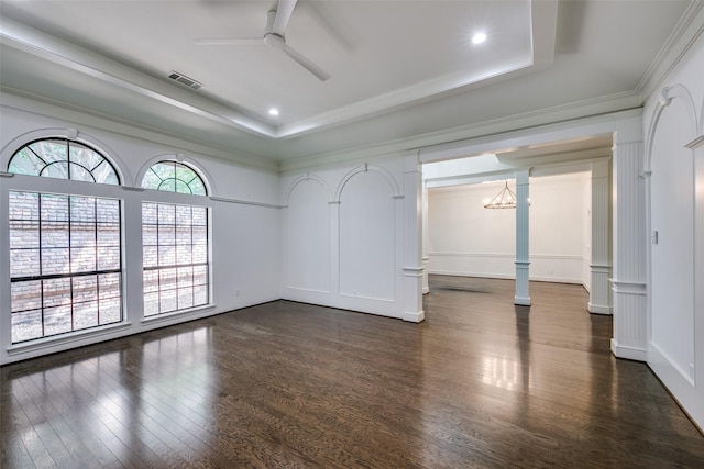 unfurnished room with a tray ceiling, ornate columns, dark wood-type flooring, and ceiling fan with notable chandelier