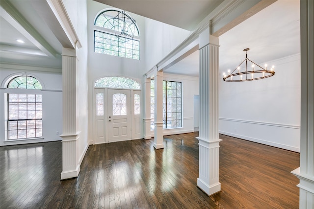 foyer with a wealth of natural light, decorative columns, dark hardwood / wood-style floors, and a notable chandelier