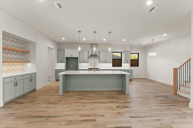 kitchen featuring pendant lighting, wall chimney exhaust hood, sink, and light hardwood / wood-style flooring