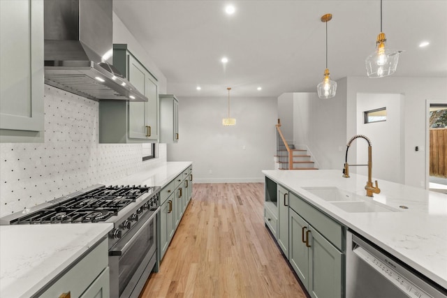 kitchen featuring sink, wall chimney exhaust hood, decorative light fixtures, light stone counters, and stainless steel appliances