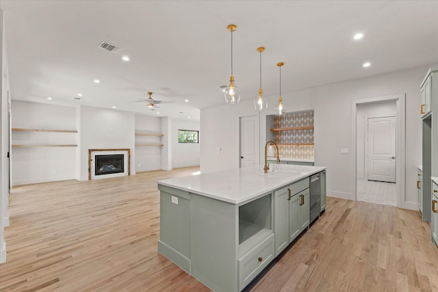 kitchen with a kitchen island with sink, ceiling fan, sink, decorative light fixtures, and light hardwood / wood-style flooring