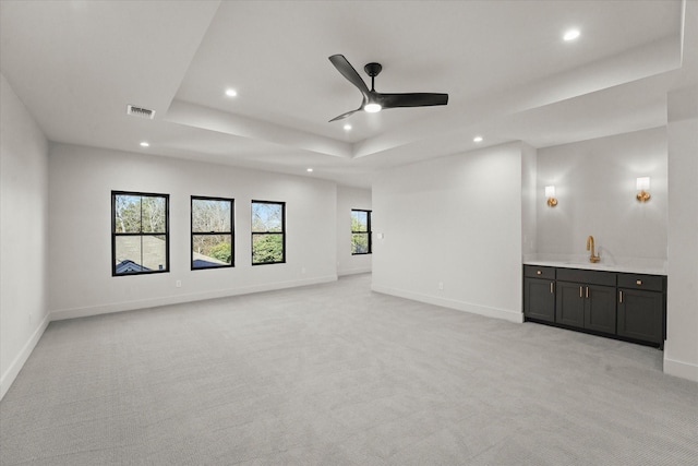 carpeted spare room featuring a raised ceiling, ceiling fan, and sink