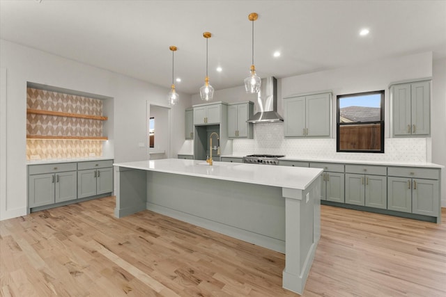 kitchen featuring sink, wall chimney exhaust hood, pendant lighting, light hardwood / wood-style floors, and decorative backsplash