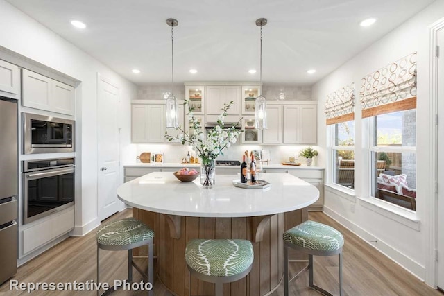 kitchen with pendant lighting, hardwood / wood-style flooring, appliances with stainless steel finishes, a kitchen island, and a kitchen bar