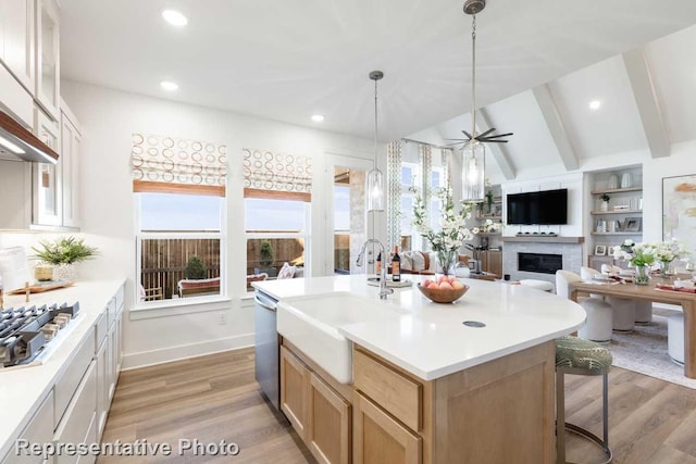 kitchen with a center island with sink, lofted ceiling with beams, sink, hardwood / wood-style flooring, and appliances with stainless steel finishes