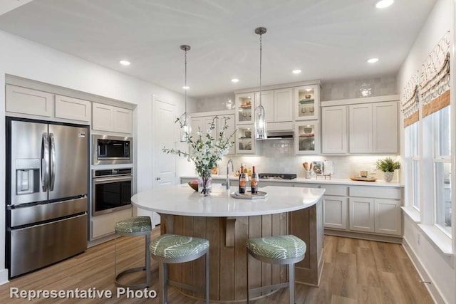 kitchen featuring a breakfast bar, a kitchen island with sink, hanging light fixtures, stainless steel appliances, and light wood-type flooring