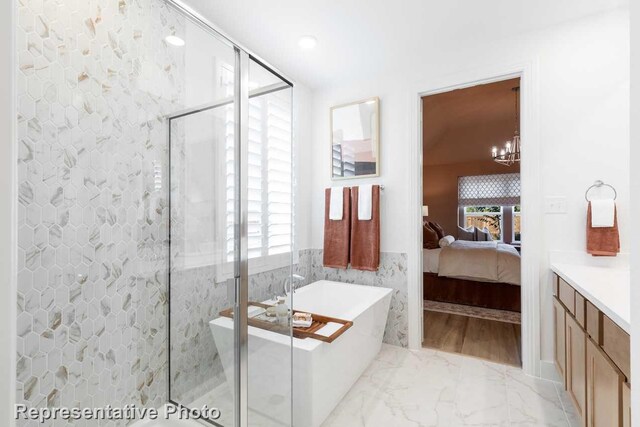 bathroom featuring vanity, tile walls, shower with separate bathtub, and an inviting chandelier