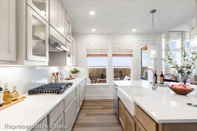 kitchen featuring dark wood-type flooring, sink, hanging light fixtures, appliances with stainless steel finishes, and decorative backsplash