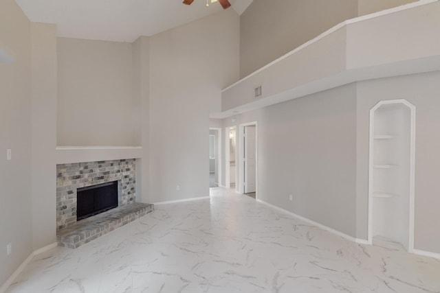 unfurnished living room featuring ceiling fan, a towering ceiling, and a brick fireplace