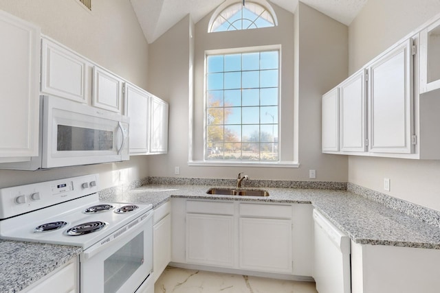 kitchen with light stone counters, white appliances, sink, white cabinetry, and lofted ceiling