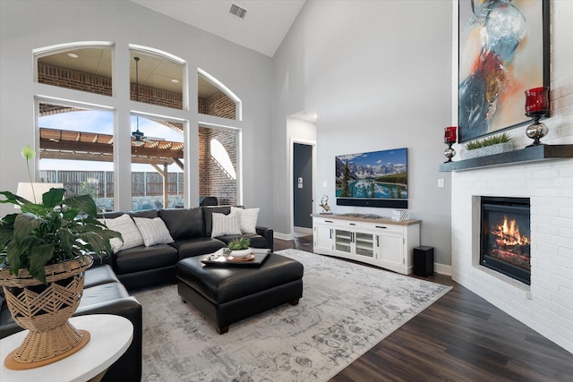 living room with visible vents, high vaulted ceiling, dark wood-style floors, a fireplace, and baseboards