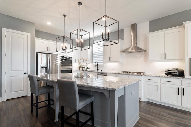 kitchen featuring a center island, wall chimney range hood, decorative light fixtures, white cabinets, and appliances with stainless steel finishes