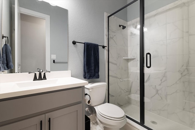 bathroom with vanity, toilet, a textured wall, and a marble finish shower