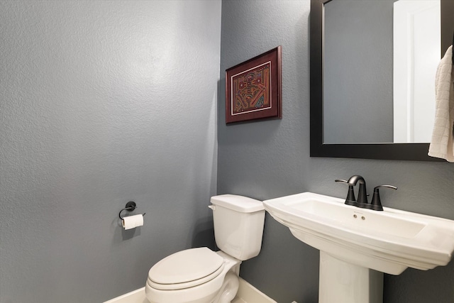 half bath featuring toilet, a textured wall, and a sink