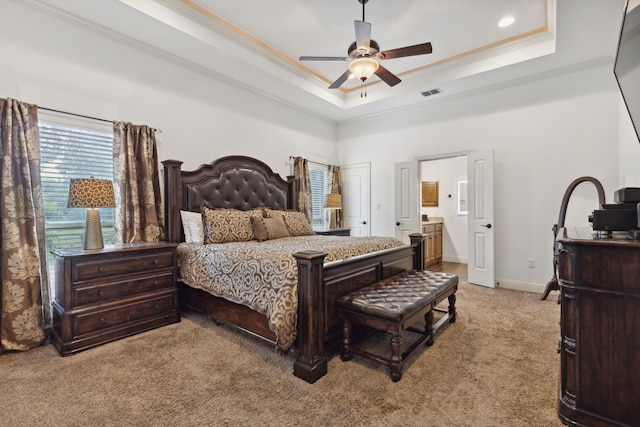 bedroom with ensuite bathroom, light carpet, ornamental molding, a tray ceiling, and ceiling fan