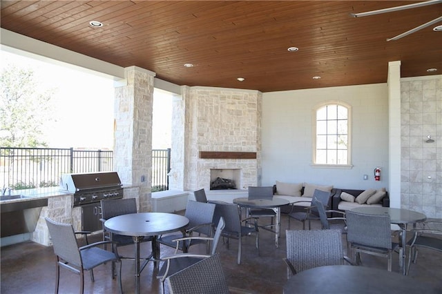 view of patio / terrace featuring exterior kitchen, ceiling fan, a grill, and an outdoor stone fireplace