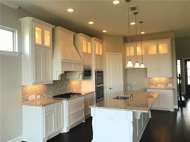 kitchen featuring white cabinets, an island with sink, hanging light fixtures, and sink