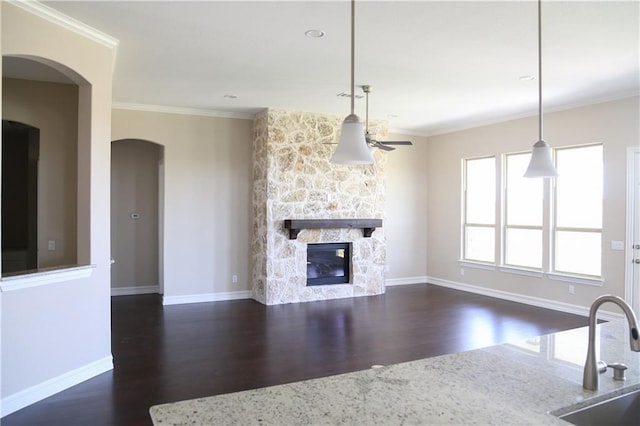 interior space with dark wood-type flooring, a stone fireplace, sink, and crown molding