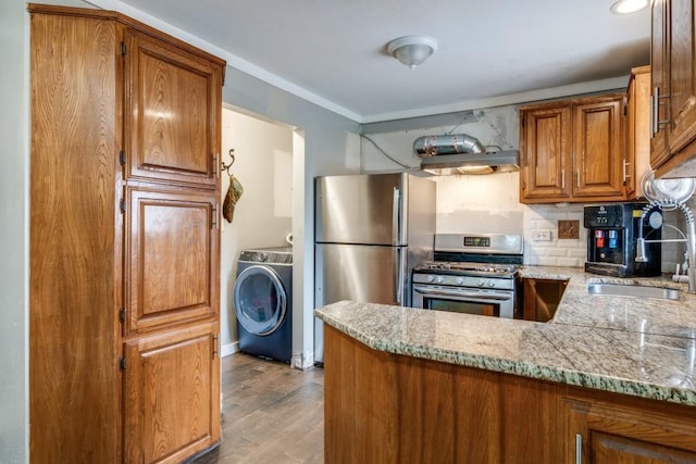 kitchen with light stone countertops, light hardwood / wood-style flooring, washer / dryer, appliances with stainless steel finishes, and sink