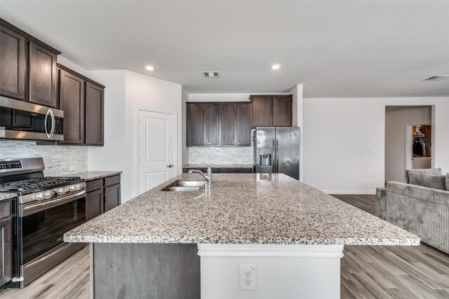 kitchen featuring decorative backsplash, appliances with stainless steel finishes, a center island with sink, and sink