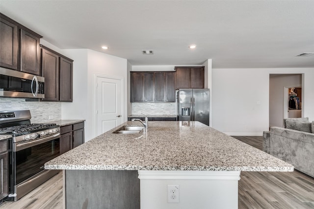 kitchen featuring stainless steel appliances, an island with sink, dark brown cabinets, and sink