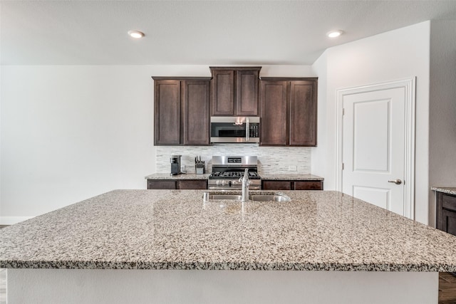 kitchen with a kitchen island with sink, dark brown cabinets, light stone counters, and appliances with stainless steel finishes