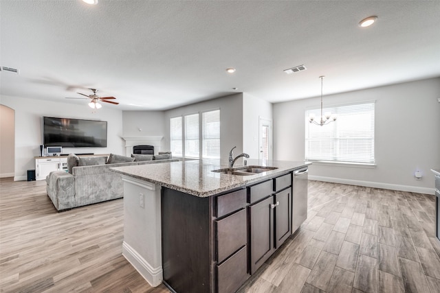 kitchen with pendant lighting, sink, dishwasher, dark brown cabinets, and light stone countertops