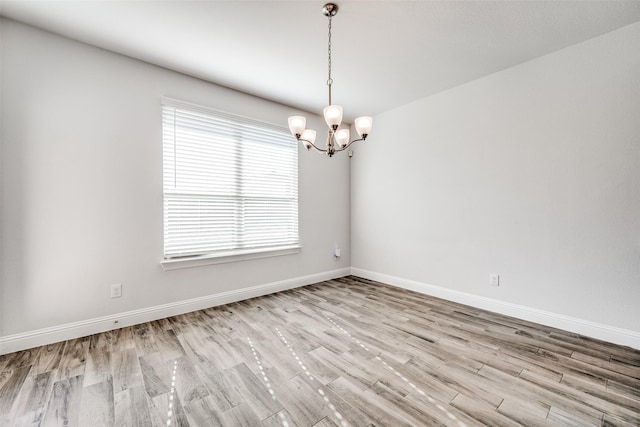 spare room featuring an inviting chandelier and light hardwood / wood-style floors