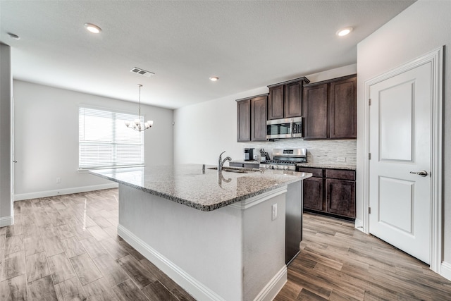 kitchen with stainless steel appliances, light stone countertops, sink, and a center island with sink