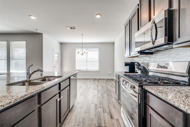 kitchen featuring sink, an inviting chandelier, light stone counters, dark brown cabinets, and appliances with stainless steel finishes