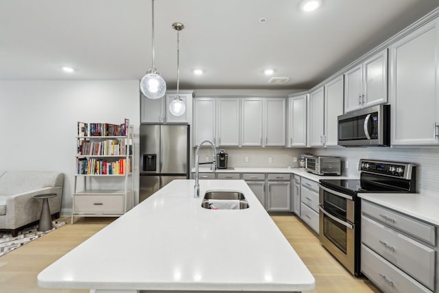 kitchen with appliances with stainless steel finishes, tasteful backsplash, an island with sink, sink, and hanging light fixtures