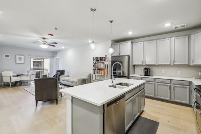 kitchen featuring decorative light fixtures, ceiling fan, gray cabinets, appliances with stainless steel finishes, and an island with sink