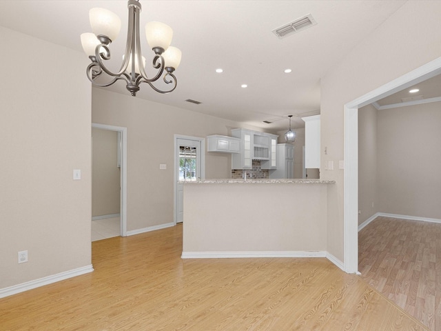 kitchen with an inviting chandelier, light hardwood / wood-style flooring, kitchen peninsula, decorative backsplash, and white cabinets