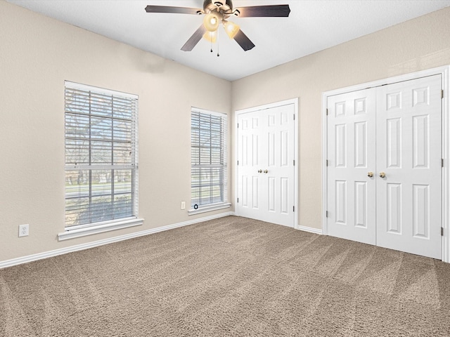 unfurnished bedroom with ceiling fan, carpet floors, multiple windows, and multiple closets