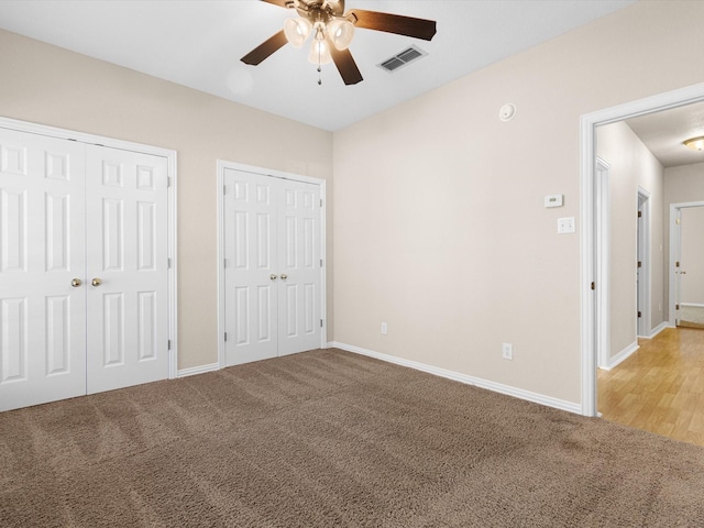 unfurnished bedroom with carpet flooring, ceiling fan, and two closets