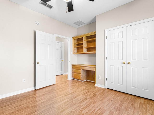 unfurnished bedroom with ceiling fan, light wood-type flooring, built in desk, and a closet