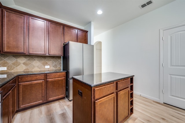 kitchen featuring decorative backsplash, stainless steel fridge, light wood-type flooring, dark stone counters, and a center island