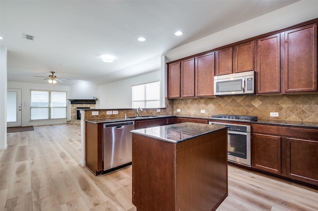 kitchen featuring appliances with stainless steel finishes, backsplash, ceiling fan, dark stone countertops, and a center island