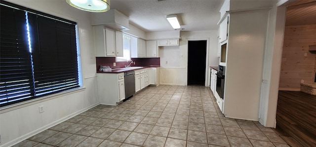 kitchen featuring white cabinets, a textured ceiling, wooden walls, light tile patterned floors, and dishwasher