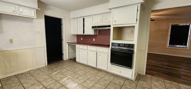 kitchen with light tile patterned flooring, white cabinets, wooden walls, and black appliances