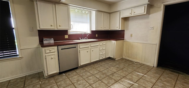 kitchen with wooden walls, dishwasher, light tile patterned floors, and sink