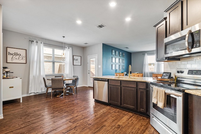 kitchen with sink, hanging light fixtures, dark brown cabinets, stainless steel appliances, and light stone counters