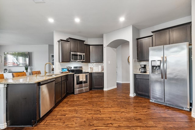 kitchen with dark brown cabinetry, sink, light stone counters, appliances with stainless steel finishes, and dark hardwood / wood-style floors