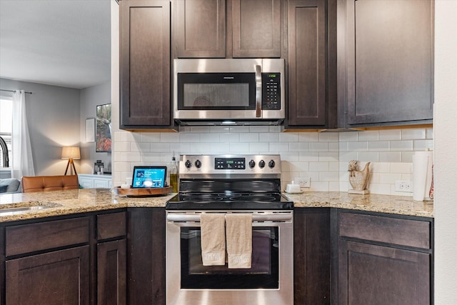 kitchen with dark brown cabinetry, stainless steel appliances, light stone countertops, and decorative backsplash